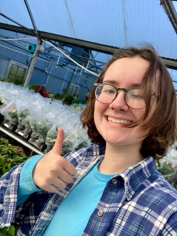 Lily giving a thumbs up inside a greenhouse