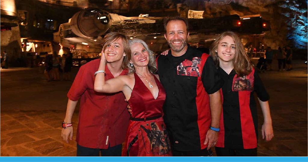 Family of four smiling in front of the Millennium Falcon model in a theme park.