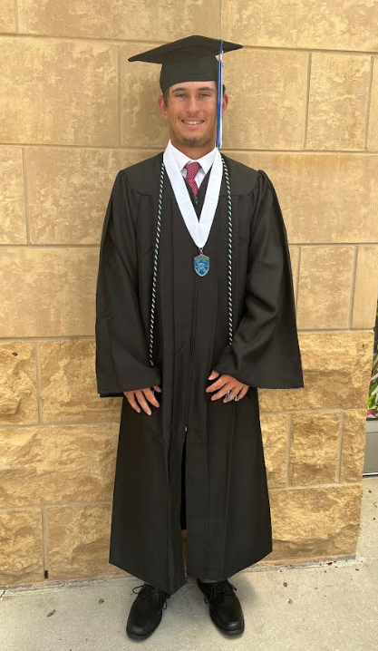 Young man in graduation attire standing against a stone wall.