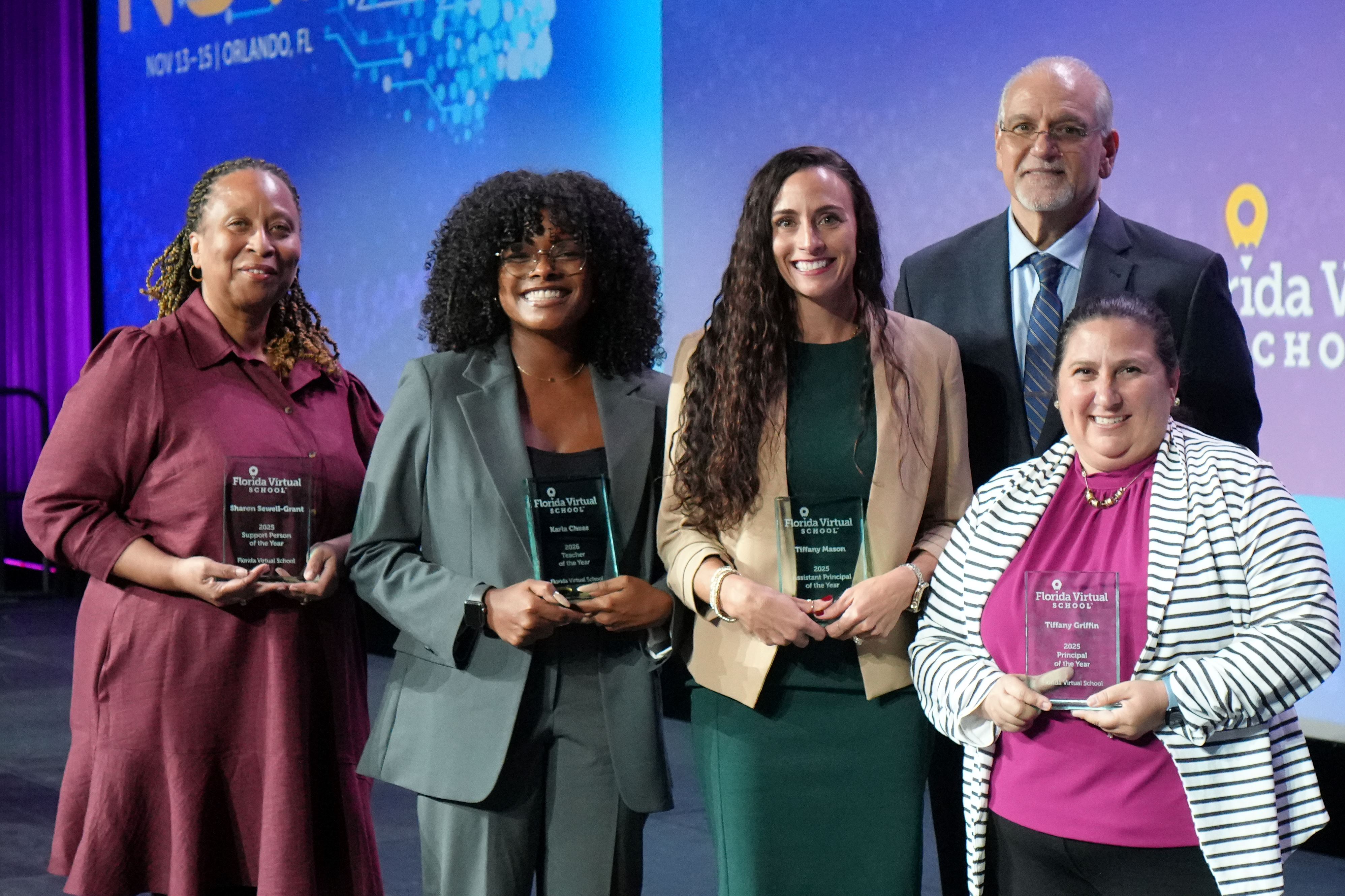 Five people holding award plaques on a stage with a blue backdrop.