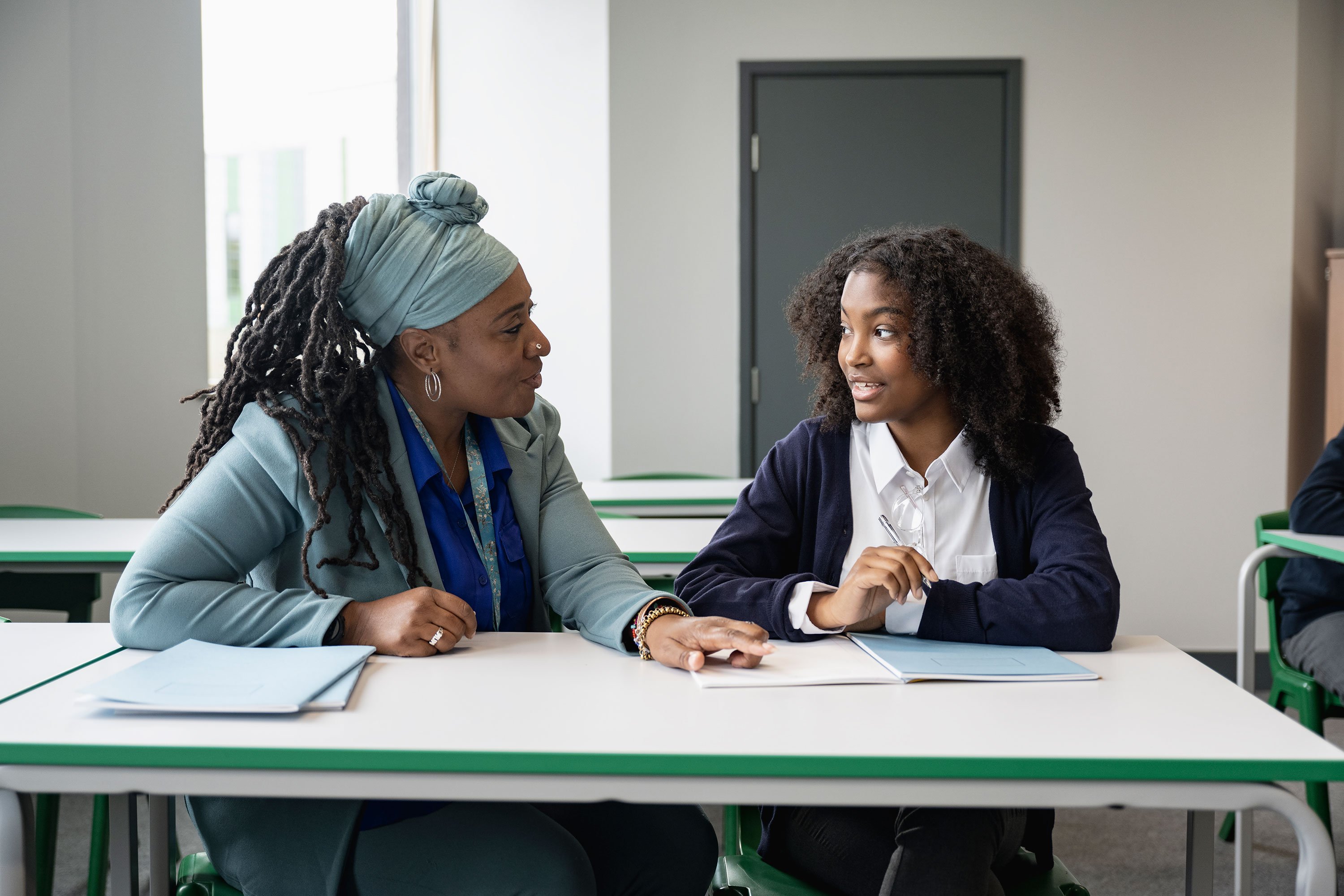 Teacher at a Department of Juvenile Justice Facility Talking to a Student at a Desk