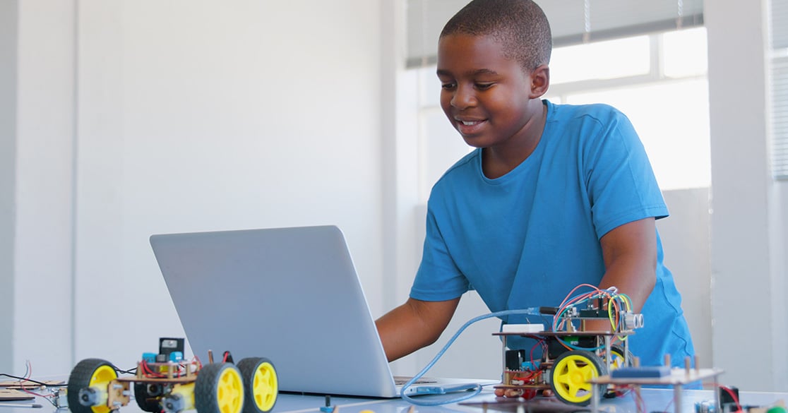 How FLVS Helps Students Earn High‑Value CTE Certifications A young student stands in front of a laptop working on his Florida Virtual School course for coding with robots on the table next to him.