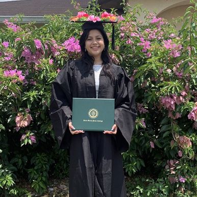 Female student, Yanet Gomez, stands in a black cap and gown at her graduation from Palm Beach State College