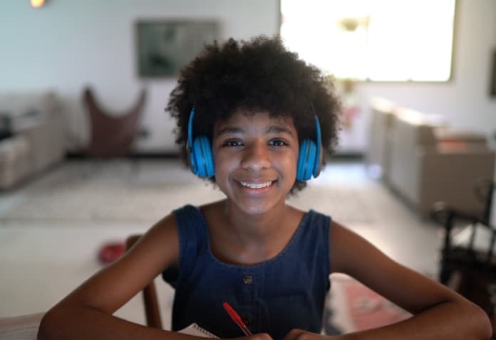 Young female FLVS Full Time Public School student smiling while participating in online learning with blue headphones on.